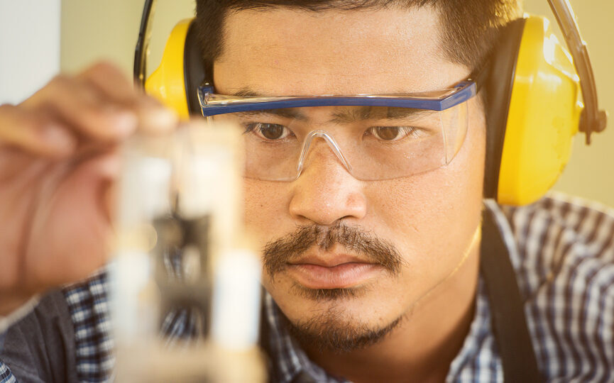A man sawing wood wearing protective eye and ear gear