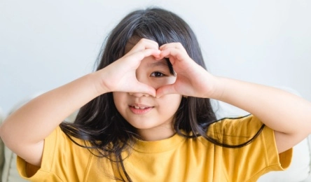 child making a hand heart around her healthy eyes